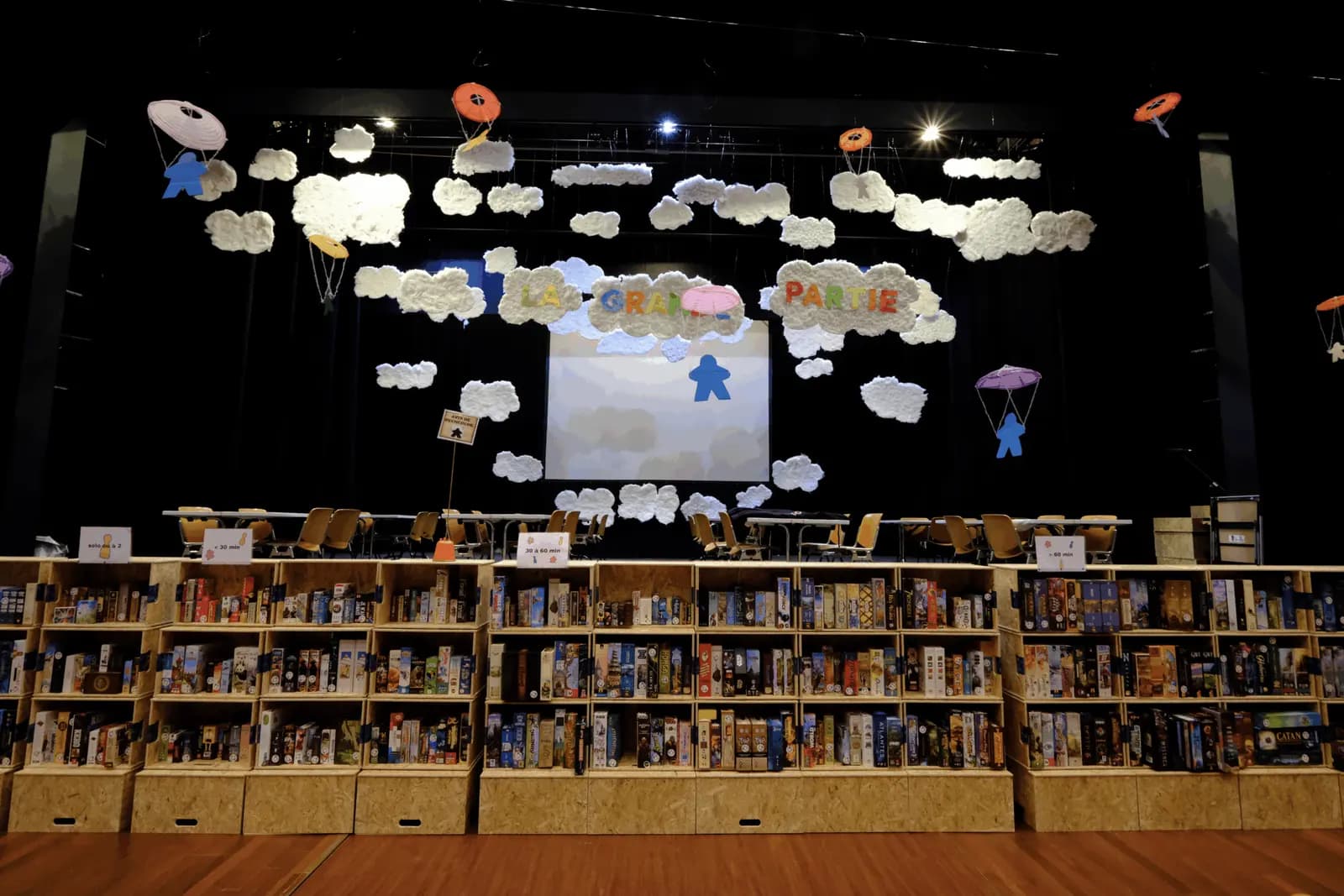 La ludothèque du festival : des étagères de jeux devant la scène décorée de nuages.