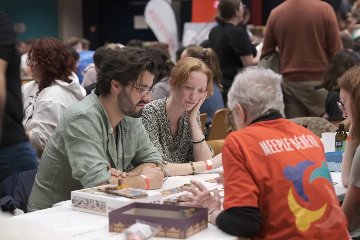 Un explicateur en t-shirt orange présente un jeu à une table de joueurs.